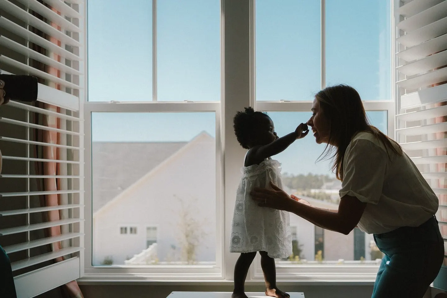 A Charlottesville family photographer silhouettes a mother touching noses with her toddler at a big window.