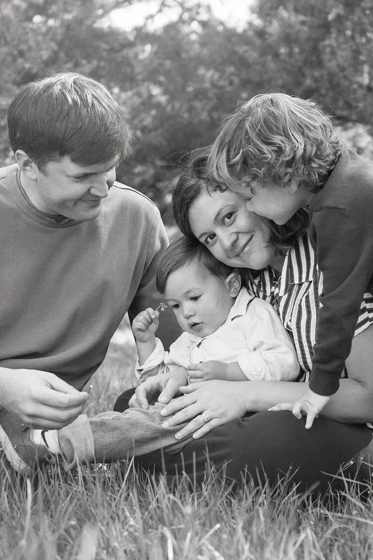 In black and white, a Charlottesville family photographer frames parents and their toddler over a tiny wildflower.