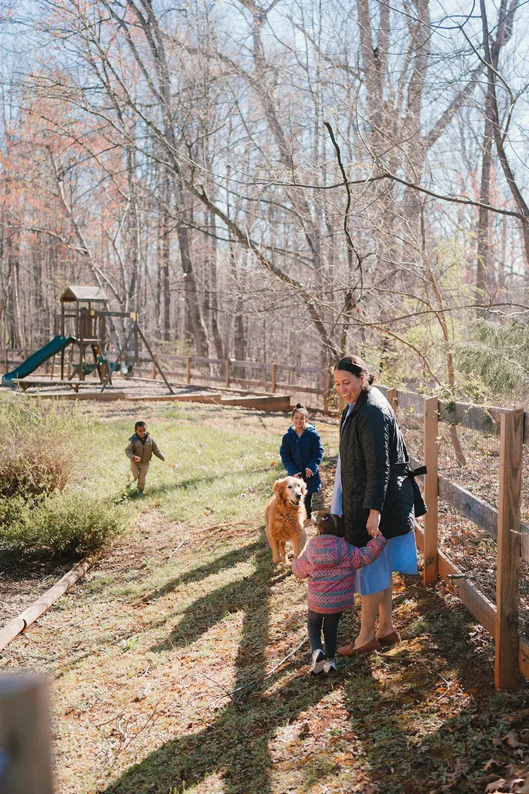 A mother and her three kids walk a wooded path with their golden retriever past a backyard playset.