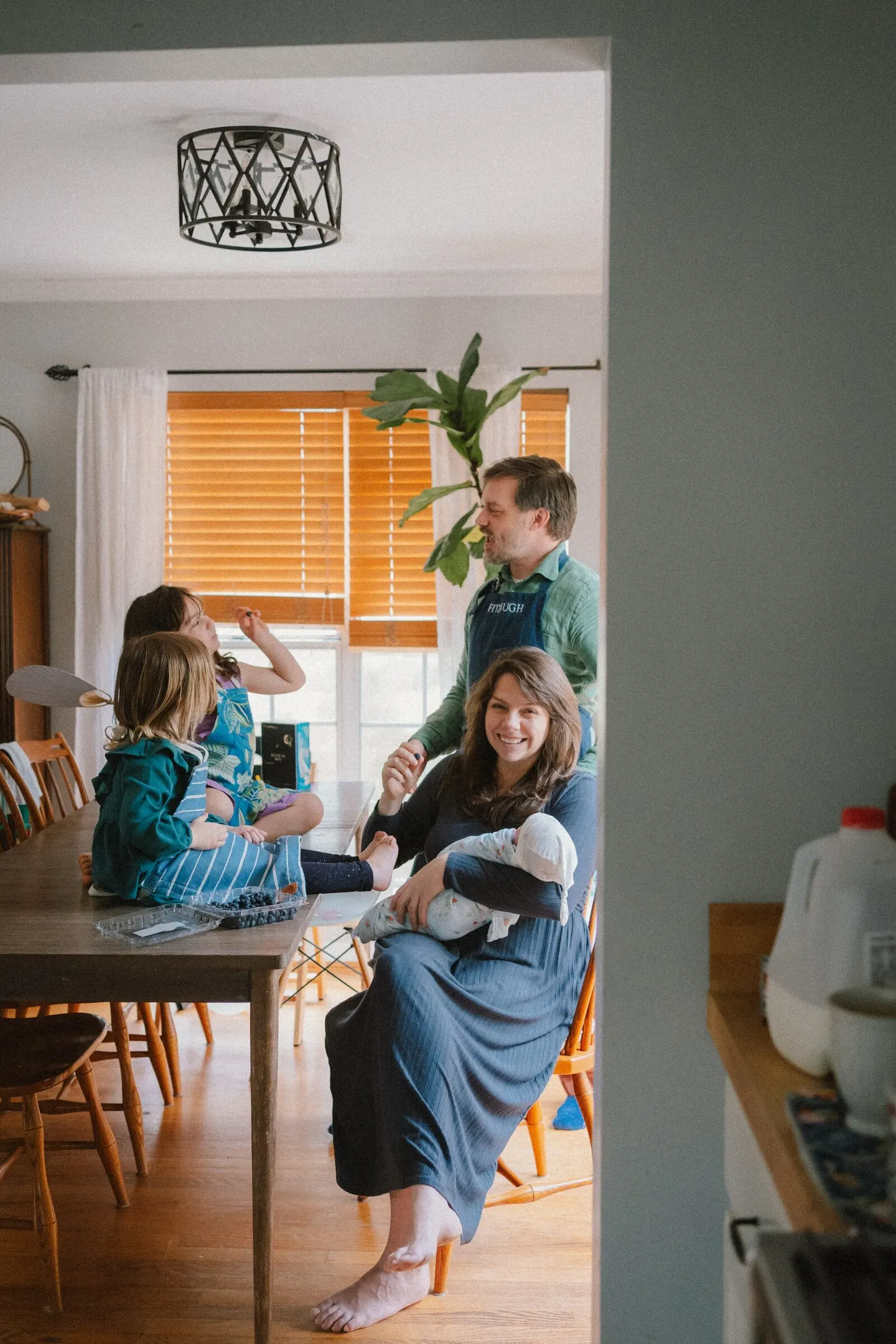 Extended family gathers around a farmhouse table with blueberries and a swaddled newborn