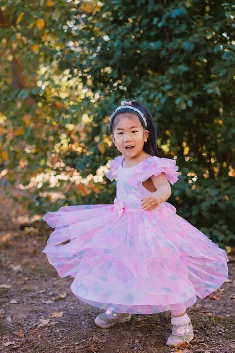 Girl twirling in a pink tulle dress on a wooded path during school photo day