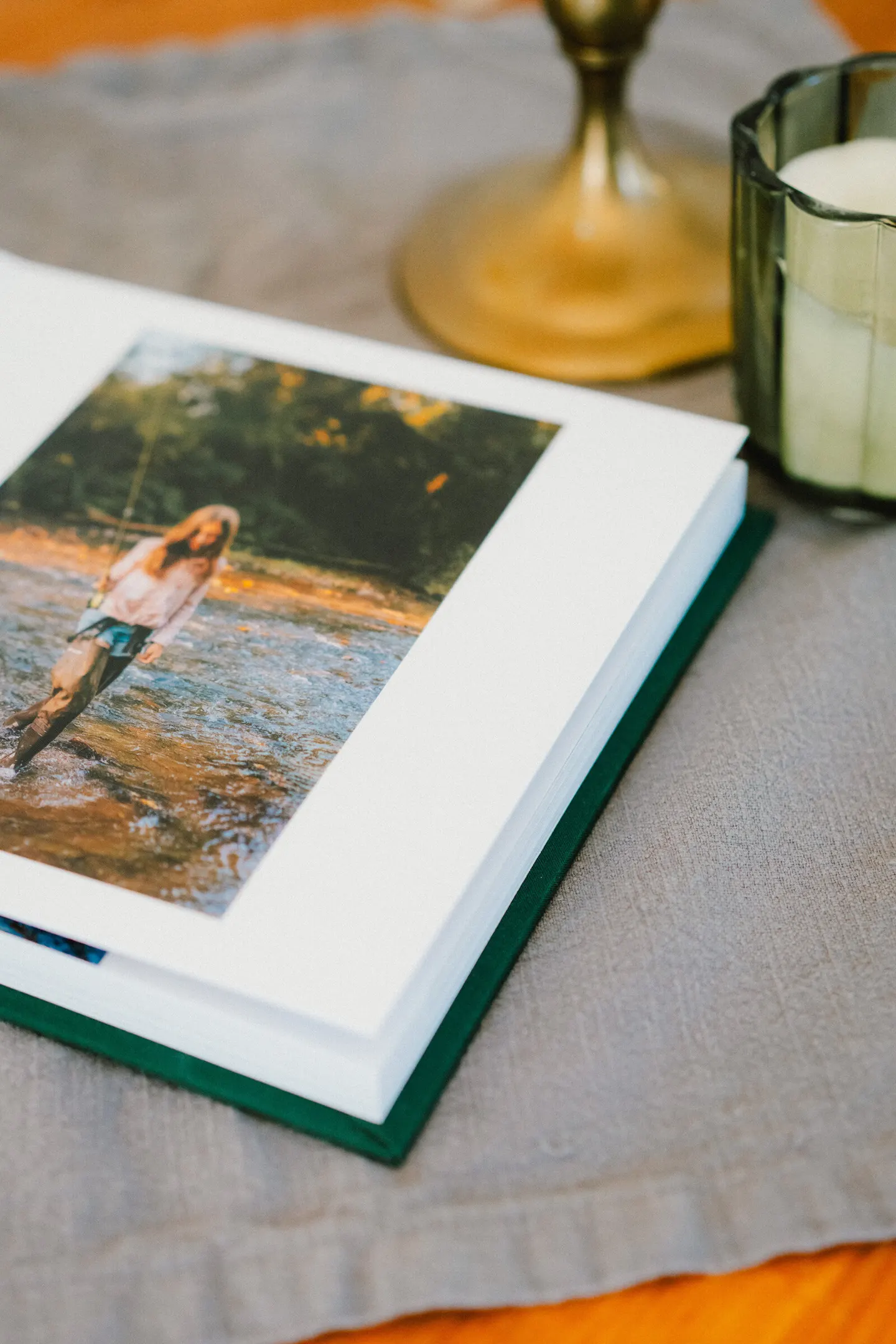 Open album spread on a linen tablecloth, a girl wading through a sunlit creek on the page