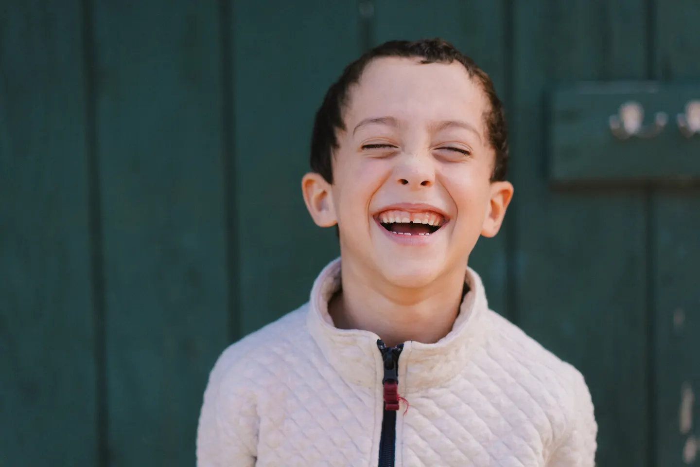Boy laughing with his eyes closed in front of a green barn door
